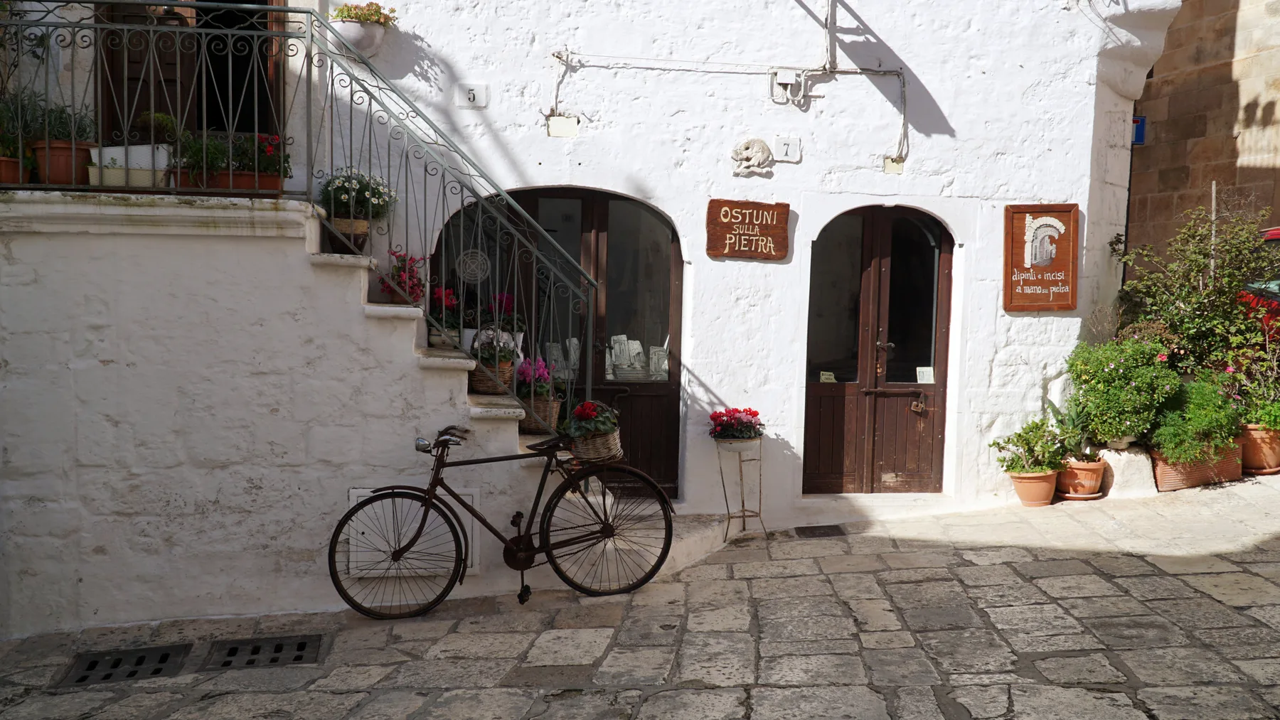 A whitewashed courtyard entrance with arched doorways, potted plants, and a bicycle.