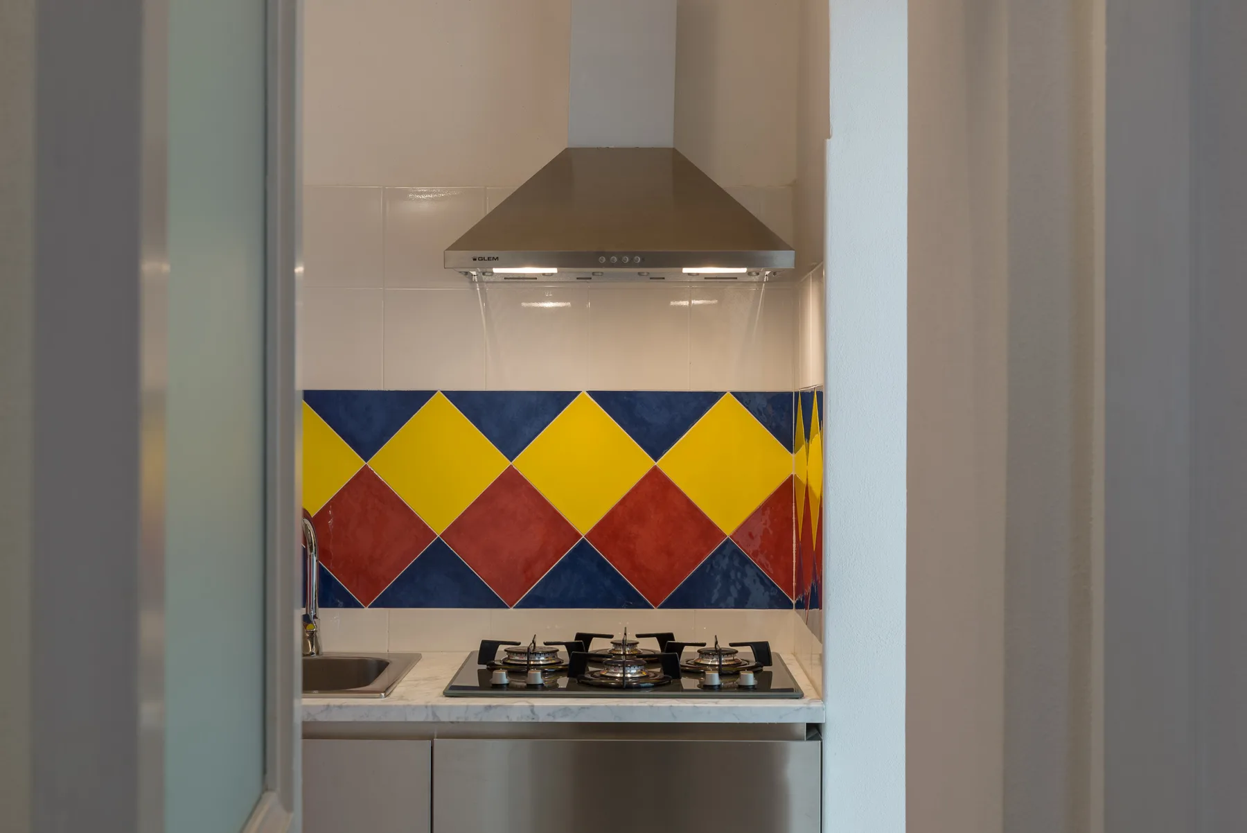 A kitchen cooktop beneath a range hood, with colorful geometric tiles behind it.