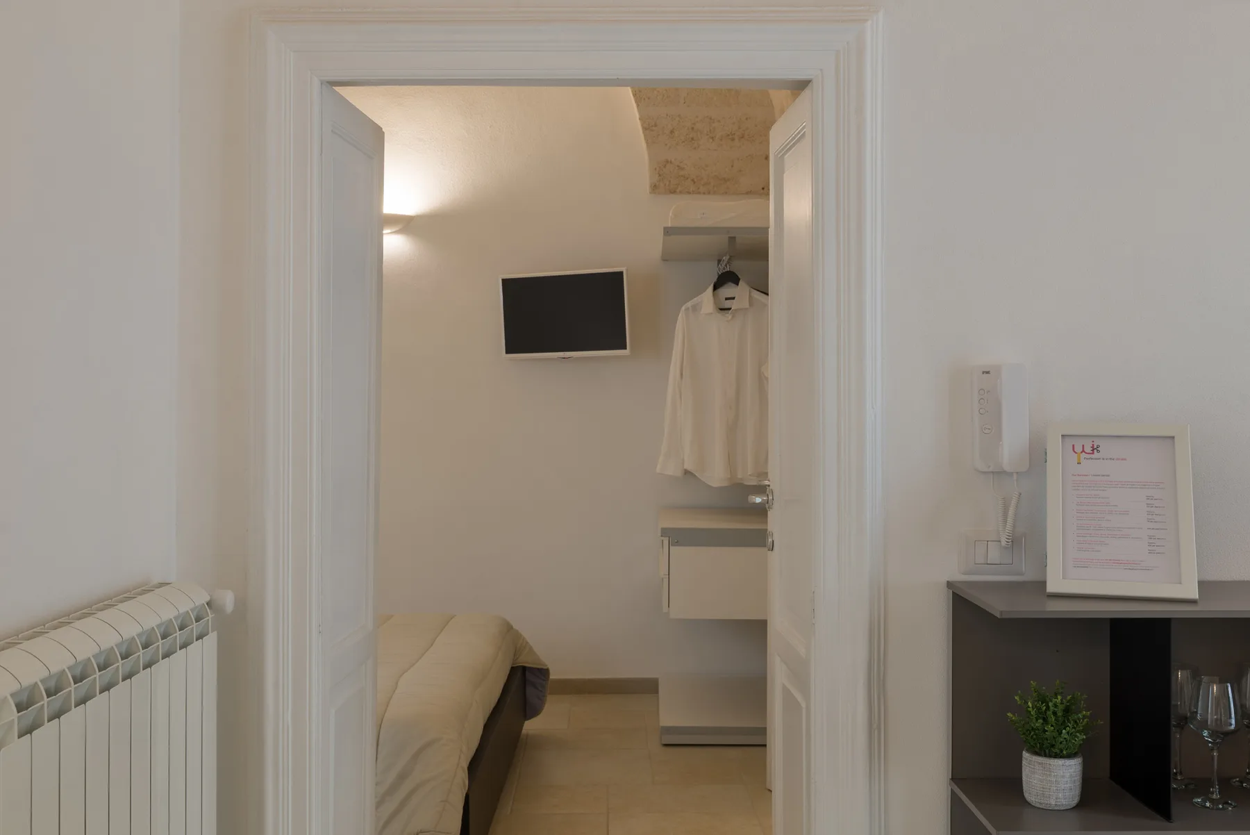 A bedroom viewed through a doorway, with a bed and wall-mounted television.