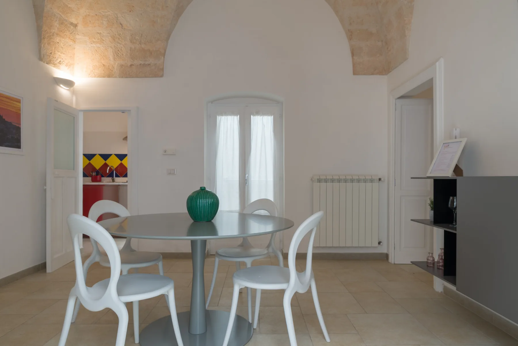 A dining area with a round table and white chairs beneath a vaulted ceiling.
