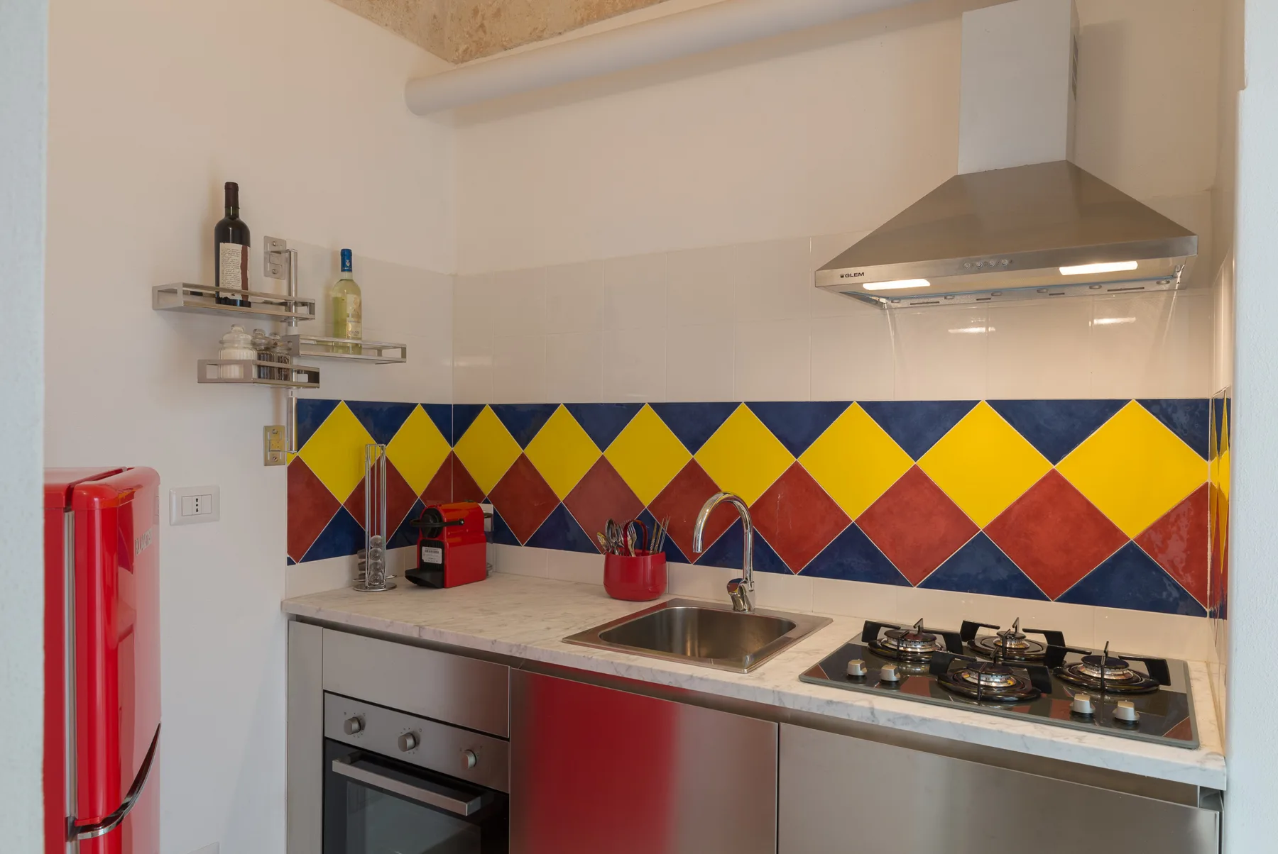 A compact kitchen with a colorful tiled backsplash, countertop, and cooking appliances.