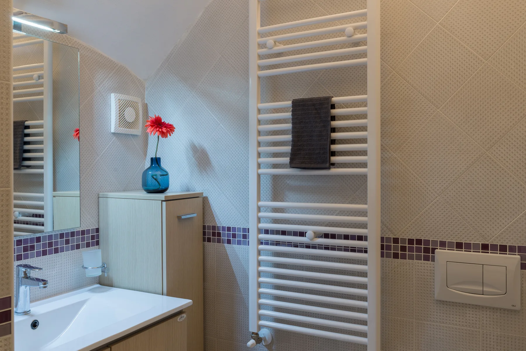 A bathroom vanity with a mirror, flowers, and a wall-mounted towel warmer.