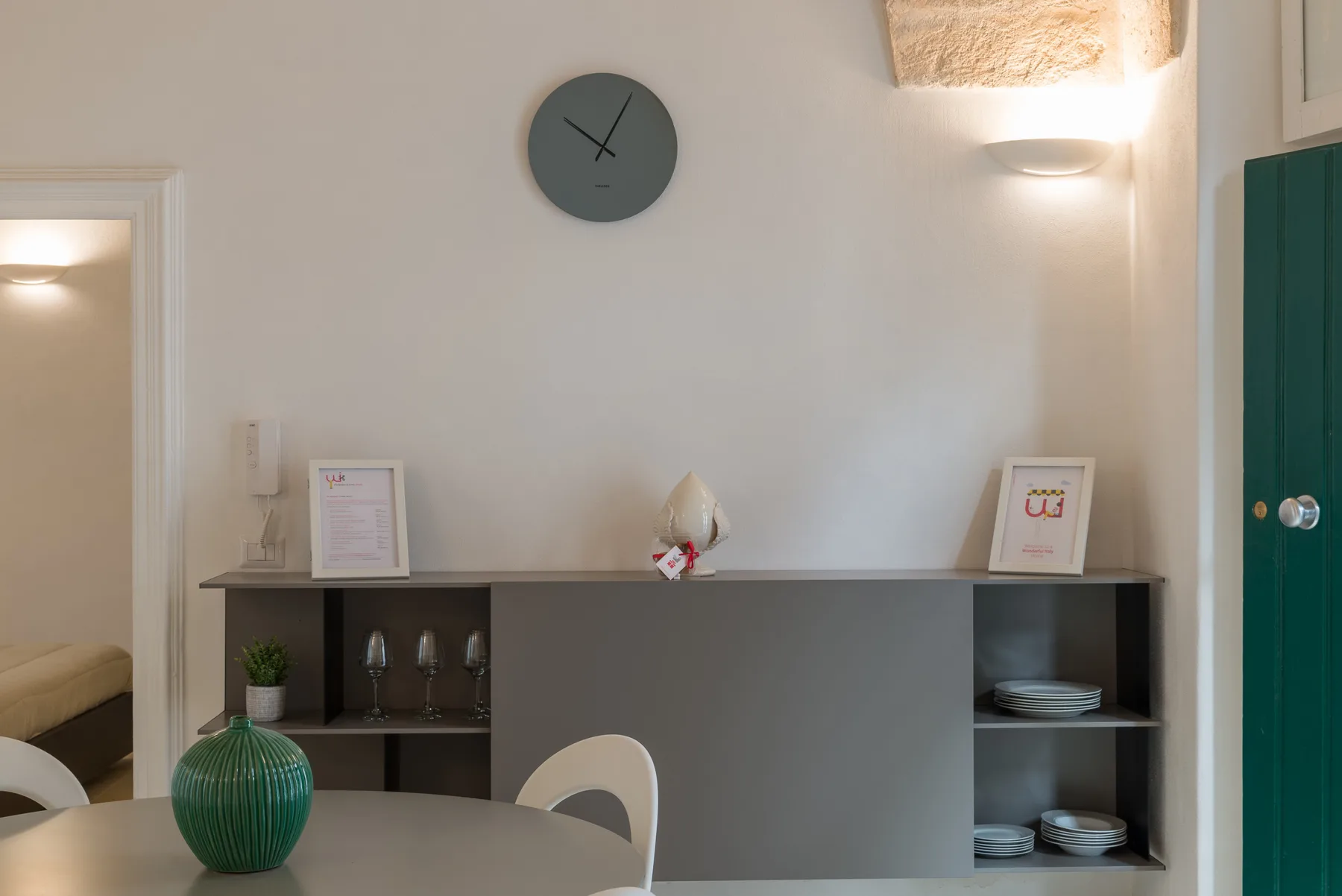 A dining area with a table, shelving, and a wall clock.