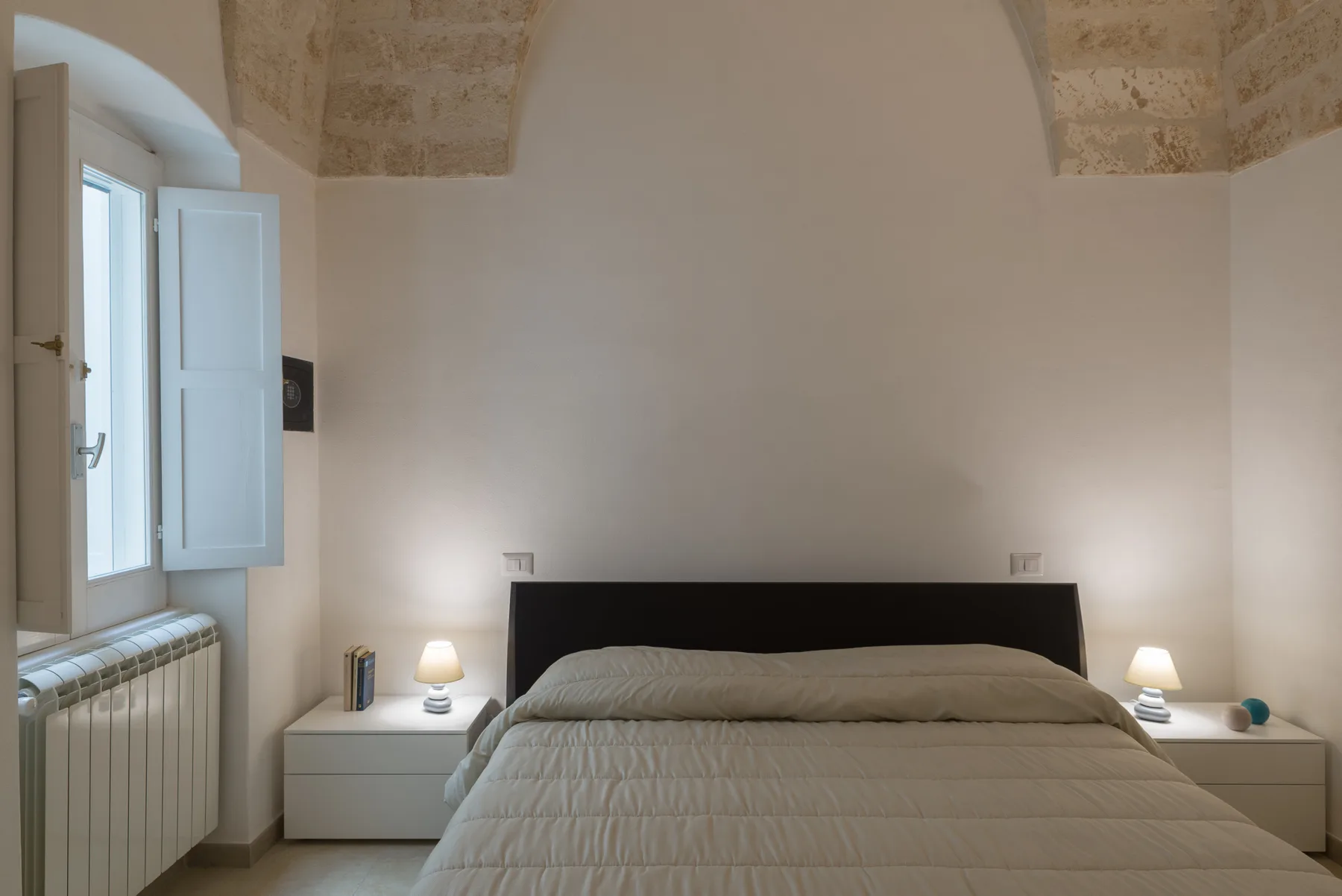 A bedroom with a neatly made bed, bedside tables, and a window.