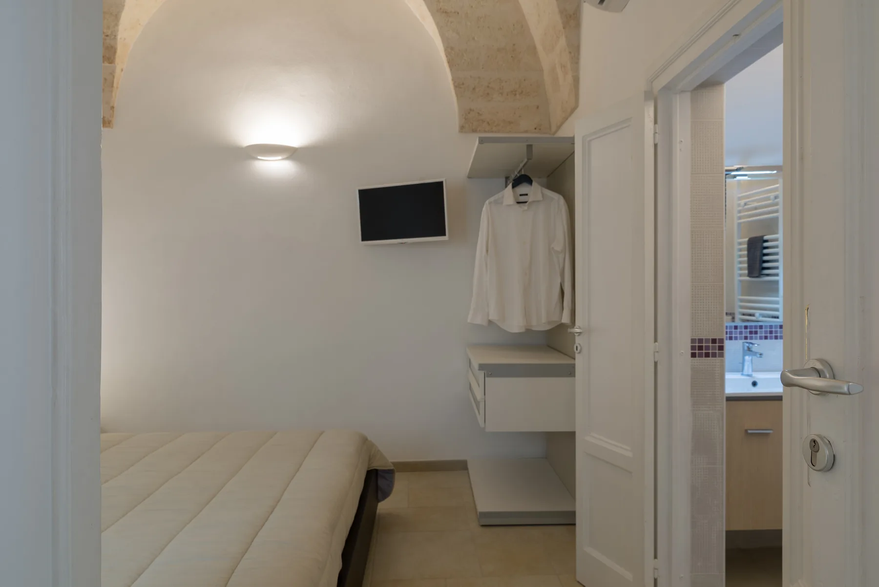 A bedroom with a bed, wall-mounted television, and an open doorway to the bathroom.