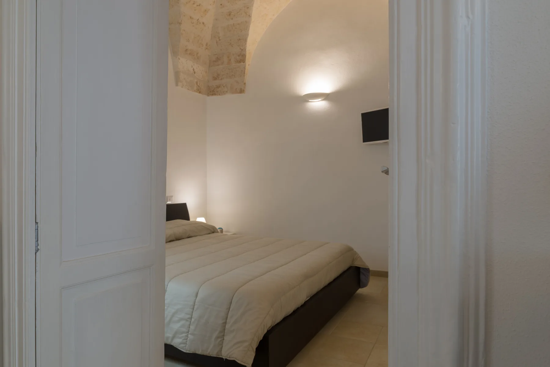 A bedroom with a neatly made bed beneath a softly lit curved ceiling.