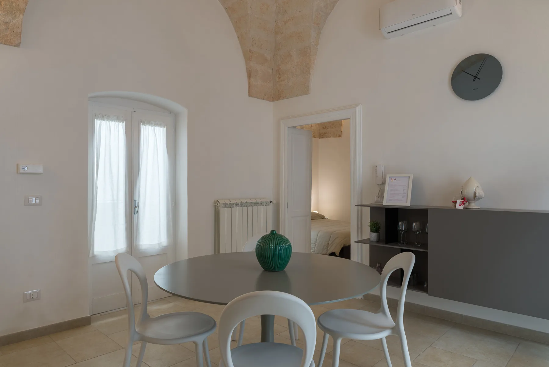 A dining area with a round table and chairs beside a curtained window.