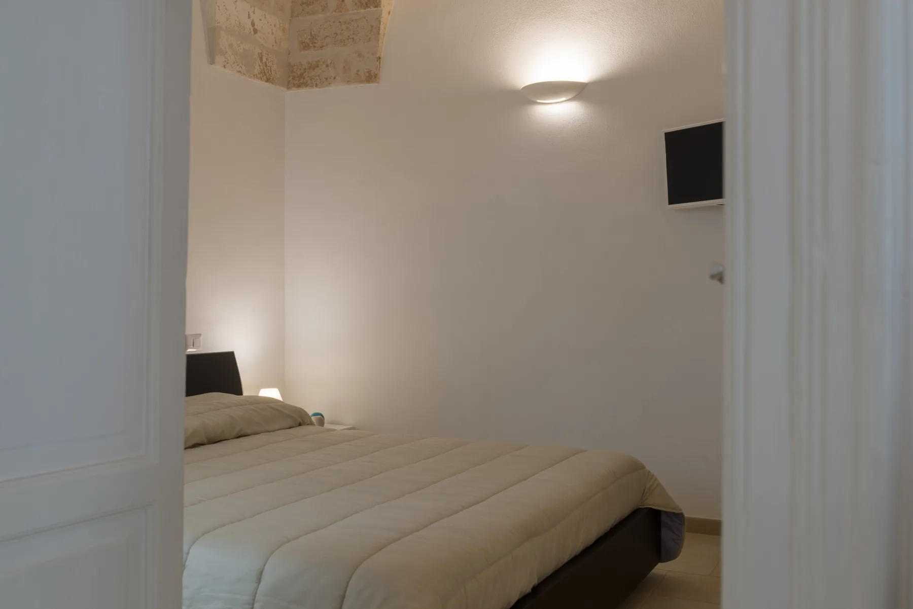 A bedroom with a neatly made bed and a wall-mounted television.