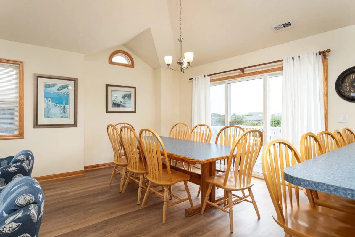 Un comedor con asientos de madera alrededor de una mesa junto a ventanas luminosas.