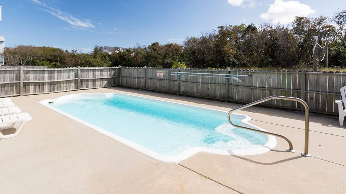 Una piscina al aire libre está junto a una terraza pavimentada y una cerca de madera.