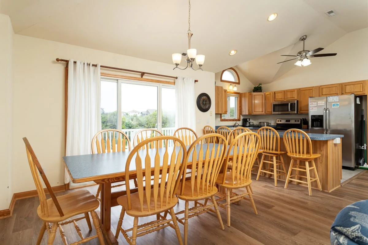 Un comedor comunica con una cocina, con asientos de madera alrededor de una mesa.