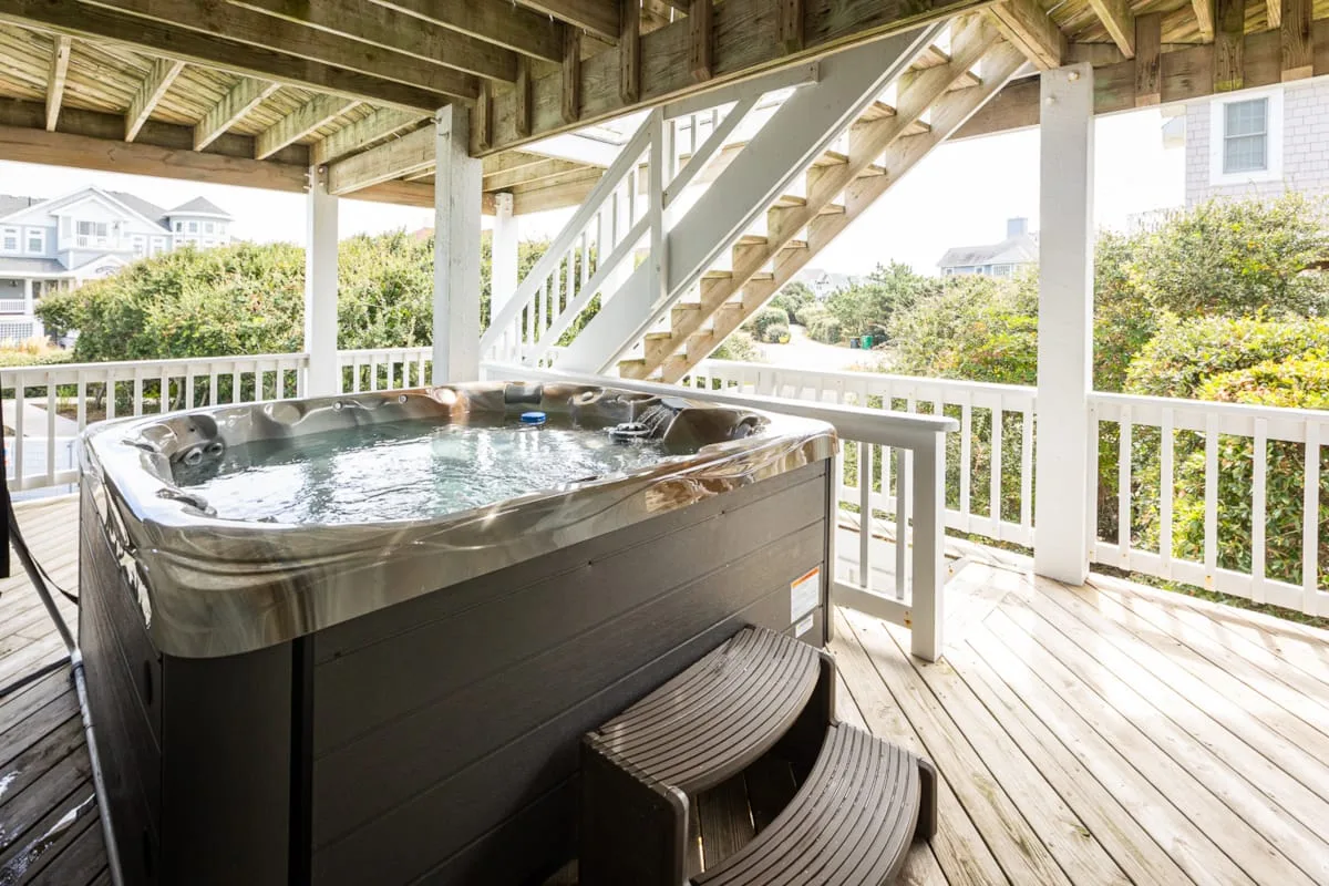 A covered outdoor deck features a large hot tub beside a staircase.