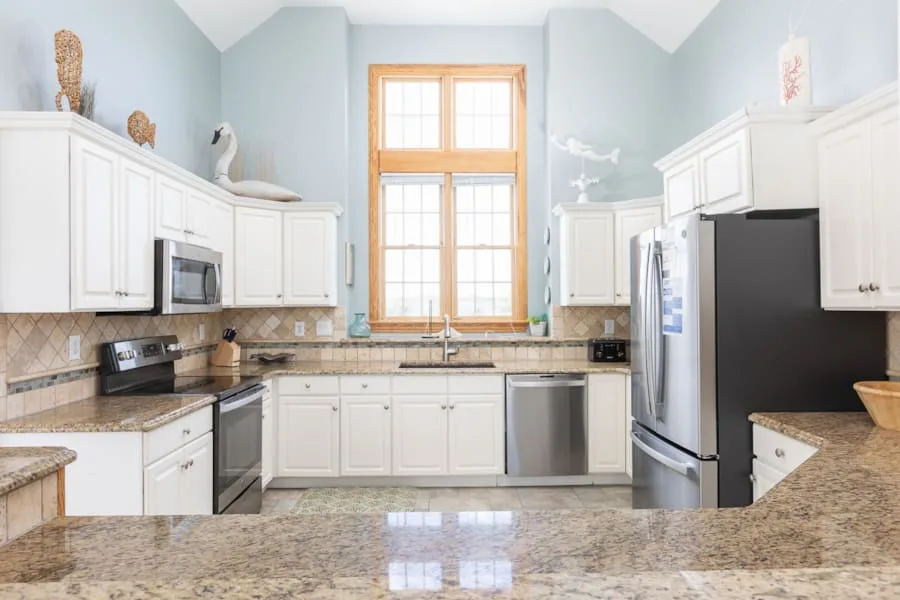 Una cocina luminosa con gabinetes blancos, electrodomésticos de acero inoxidable y una gran ventana central.
