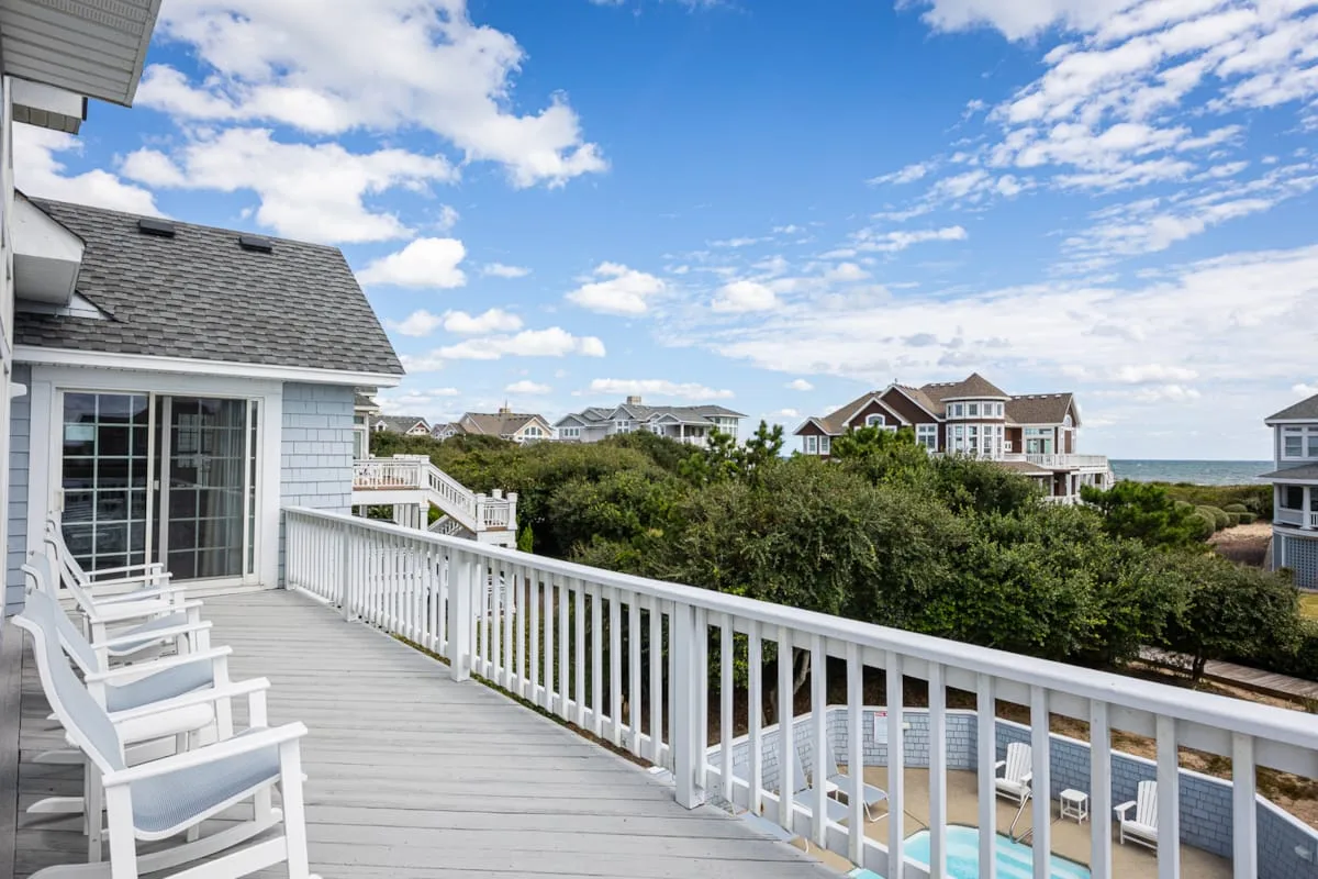 A white-railed deck overlooks greenery, nearby houses, and the ocean.