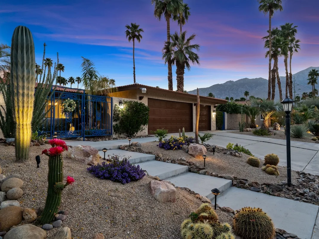 Desert landscaping and a paved path lead to a house at dusk.