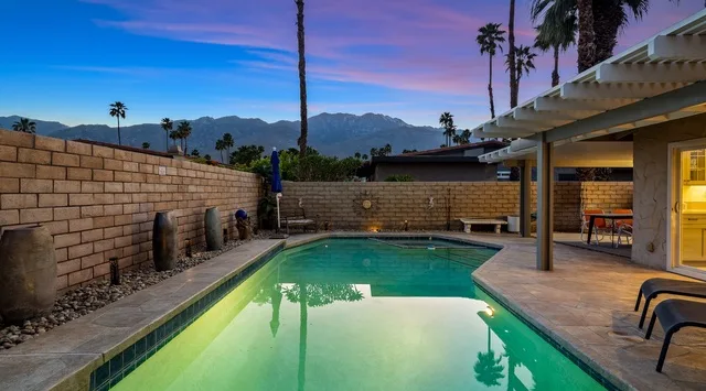 Una piscina al aire libre junto a un patio cubierto, con montañas visibles a lo lejos.