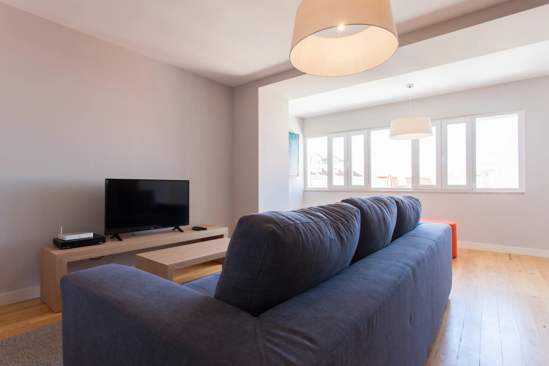 Una sala luminosa con asientos azules, un televisor y grandes ventanas.