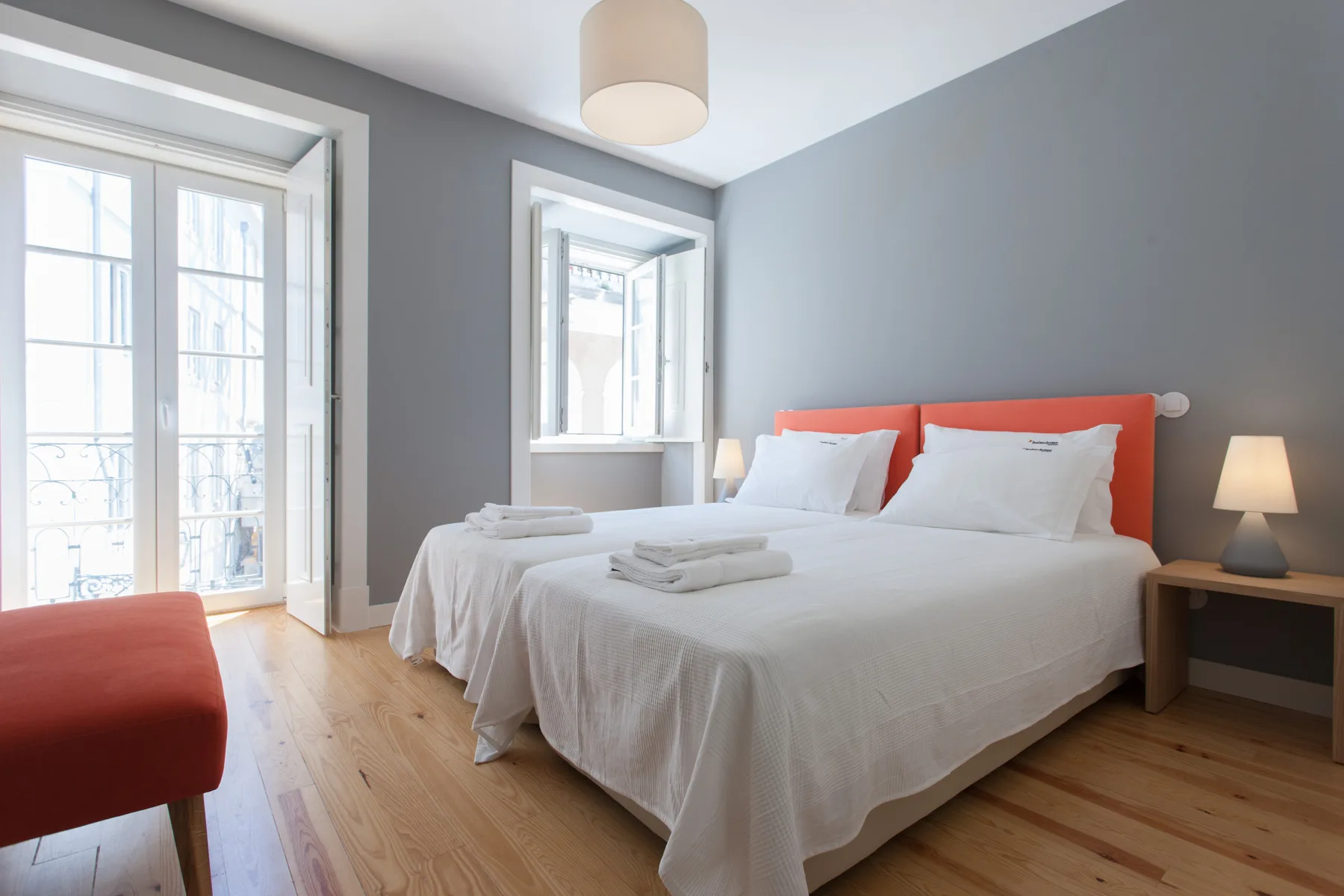 Un dormitorio luminoso con una cama bien hecha y ventanas altas.