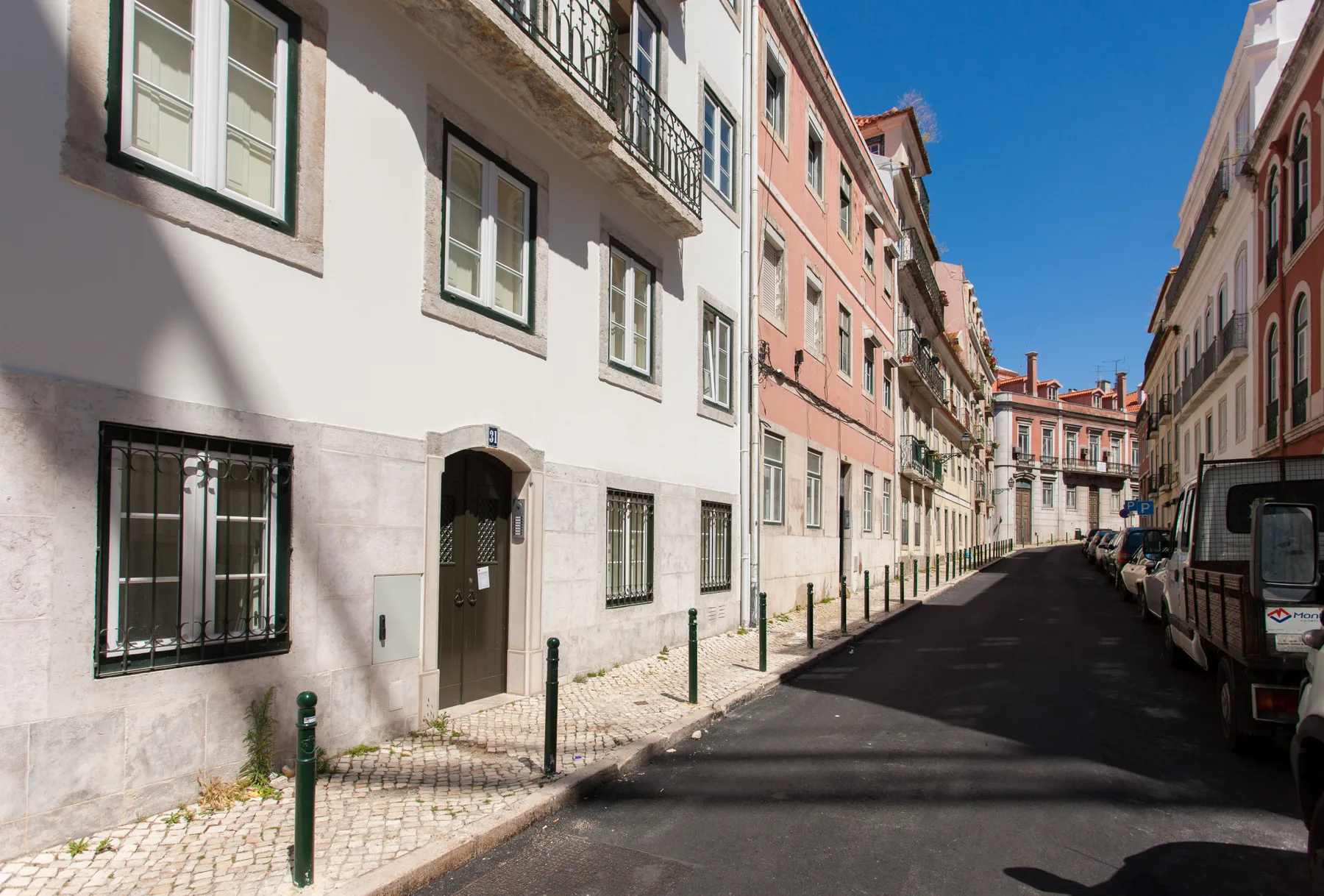 Una calle urbana estrecha bordeada de edificios de varios pisos y vehículos estacionados.