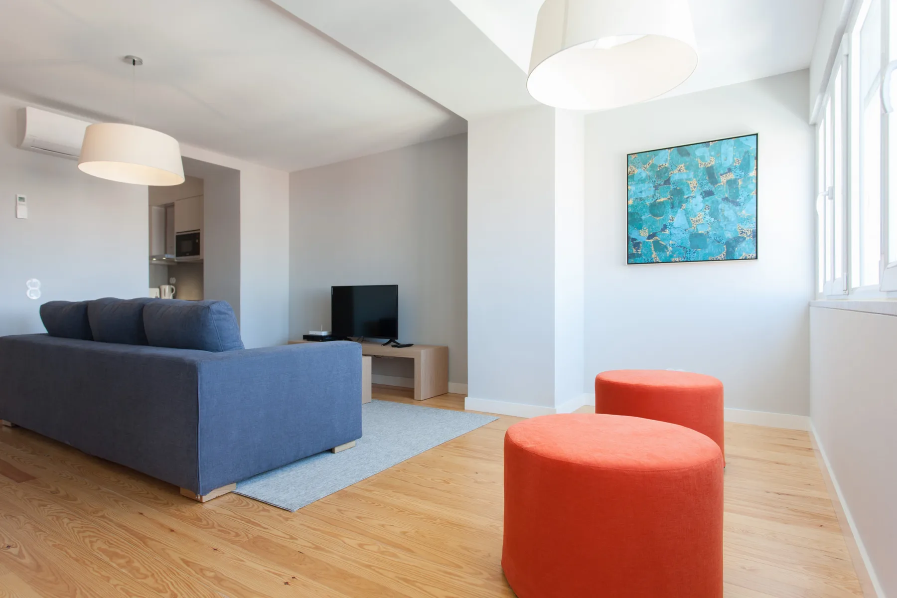Sala de estar con asientos azules, otomanas rojas y un televisor.