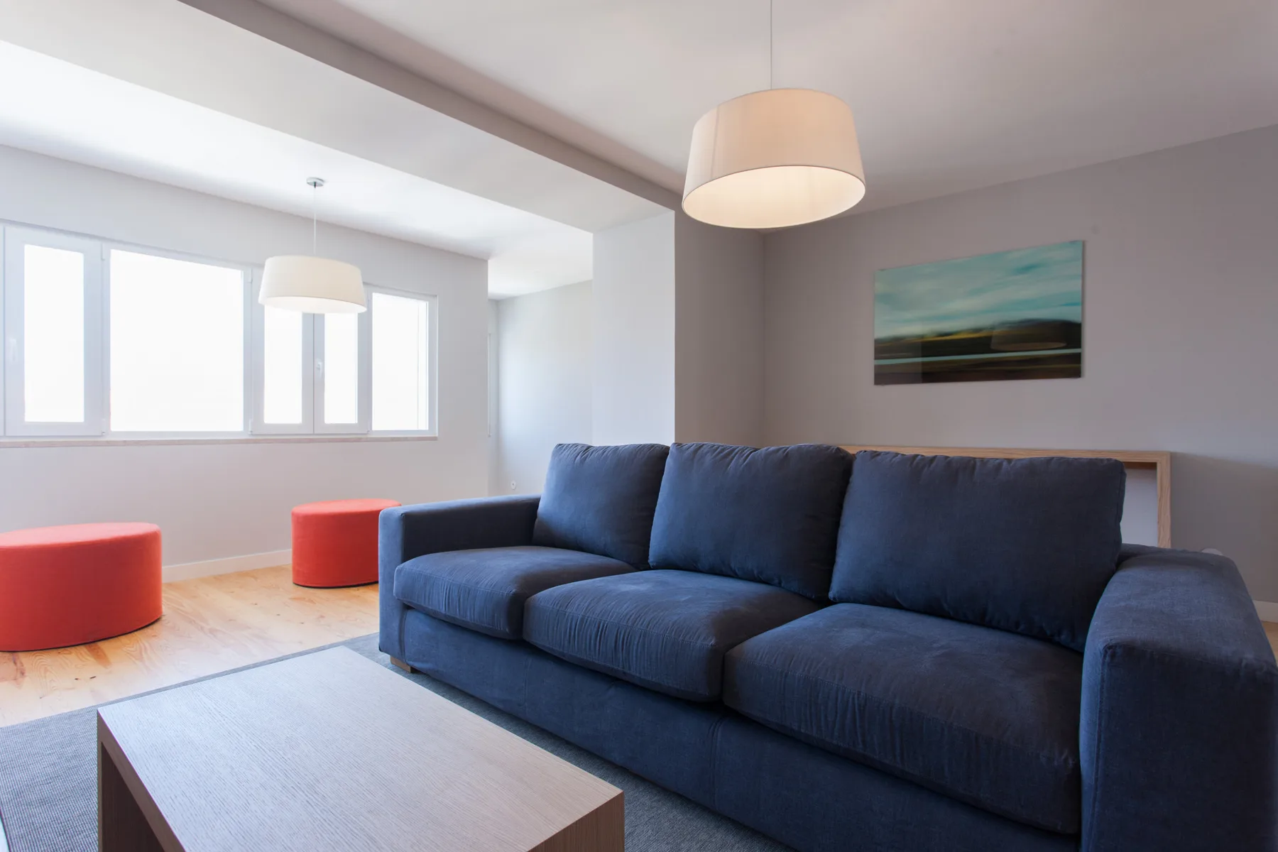 Sala de estar con asientos azules, una mesa de centro y ventanas grandes.
