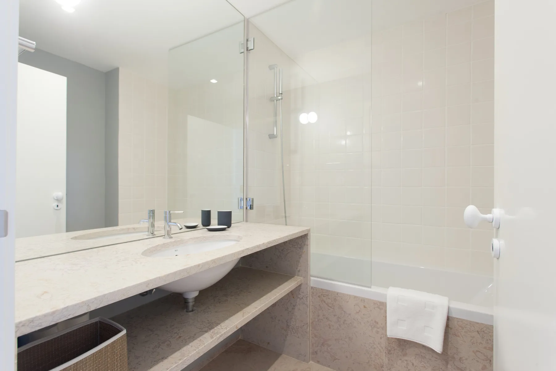 Un baño luminoso con un lavabo alargado y una mampara de ducha de vidrio.