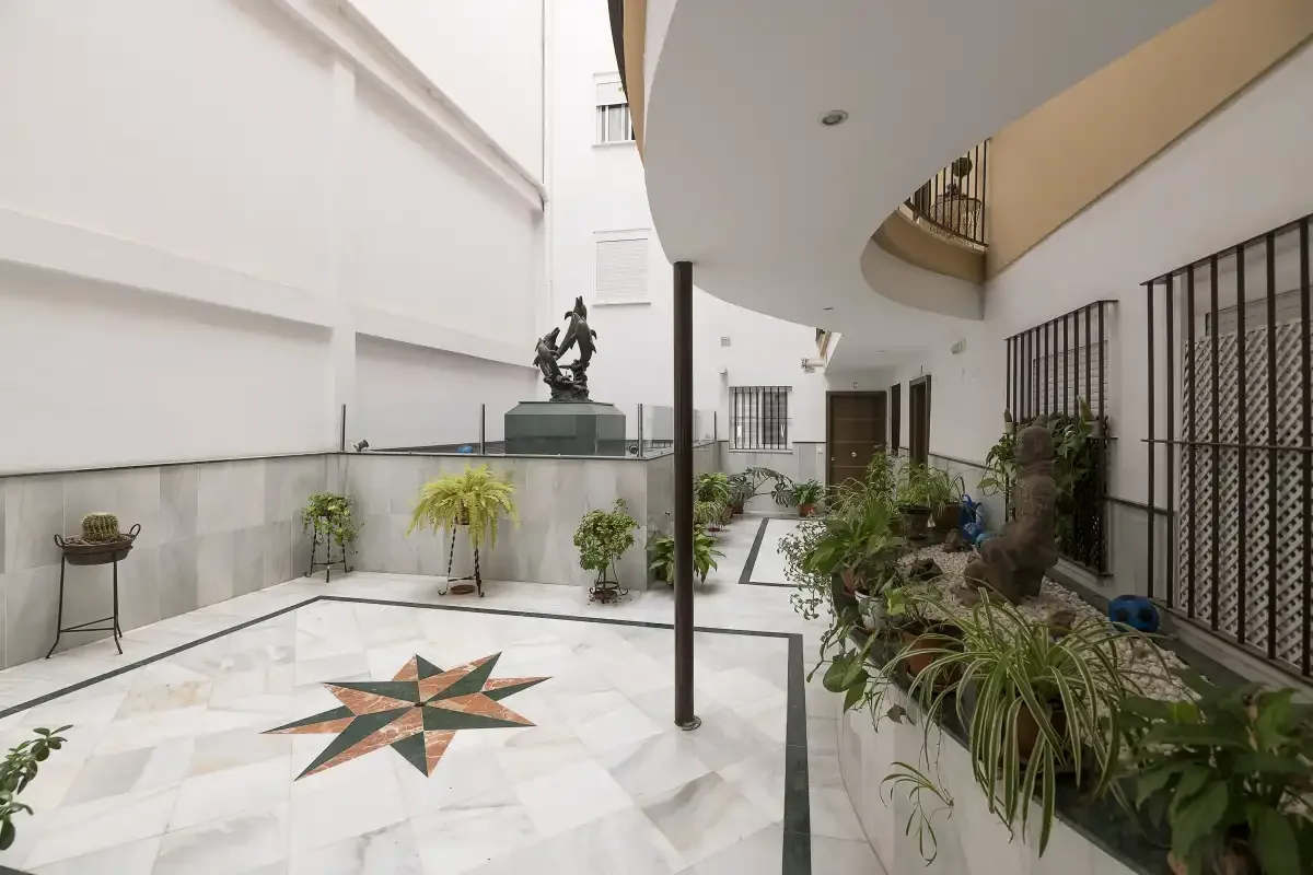 An indoor courtyard with a tiled floor, central fountain, and surrounding plants.