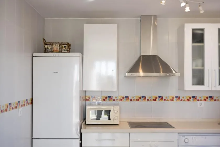 A bright kitchen with white cabinets, a refrigerator, and a stainless steel range hood.