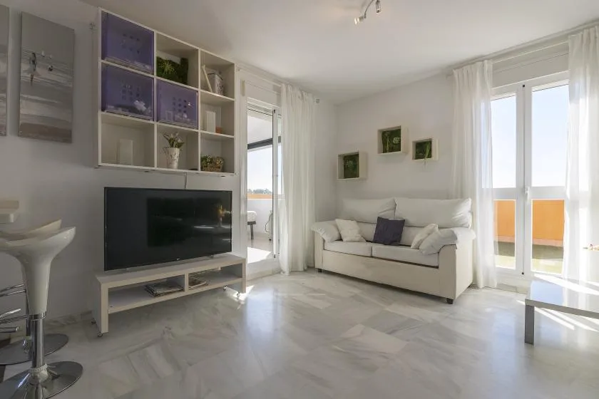 A bright living room with seating, a television, and glass doors opening onto a balcony.