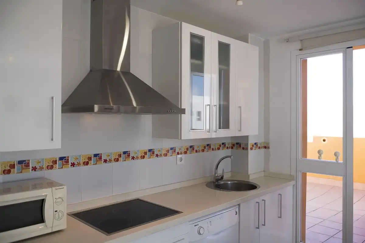 A bright kitchen with a cooktop, range hood, and a door opening onto a balcony.