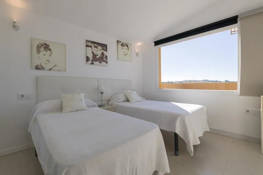 A bright bedroom with two beds beneath framed wall art.