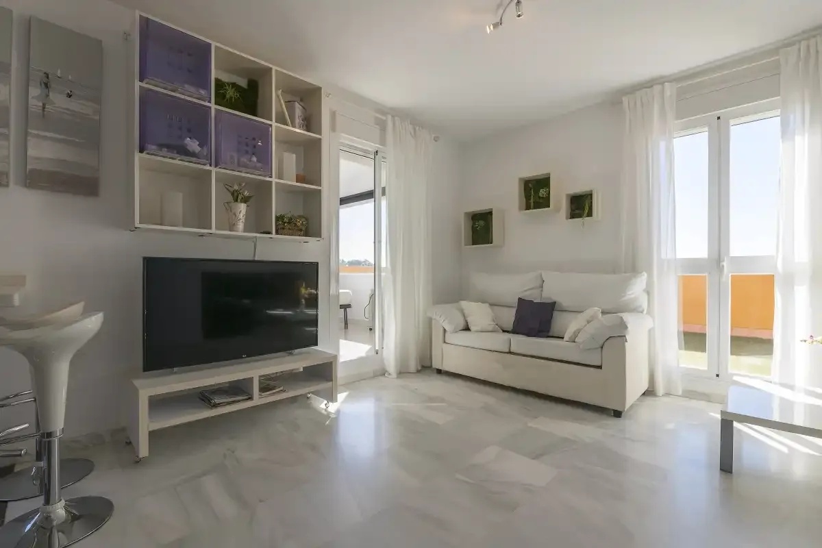 A bright living room with a sofa, television, and glass doors.