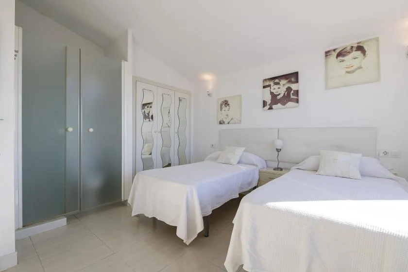A bright bedroom with two beds and framed artwork on the walls.