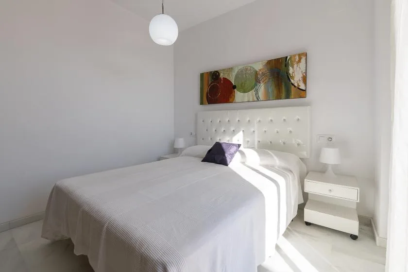 A bright bedroom with a large bed, a tufted headboard, and wall art.