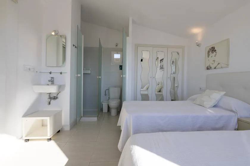 A bright bedroom with two beds and a small washbasin.