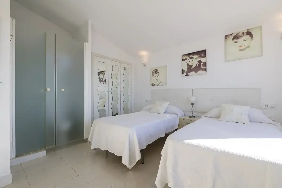 A bright bedroom with two beds and framed artwork on the walls.