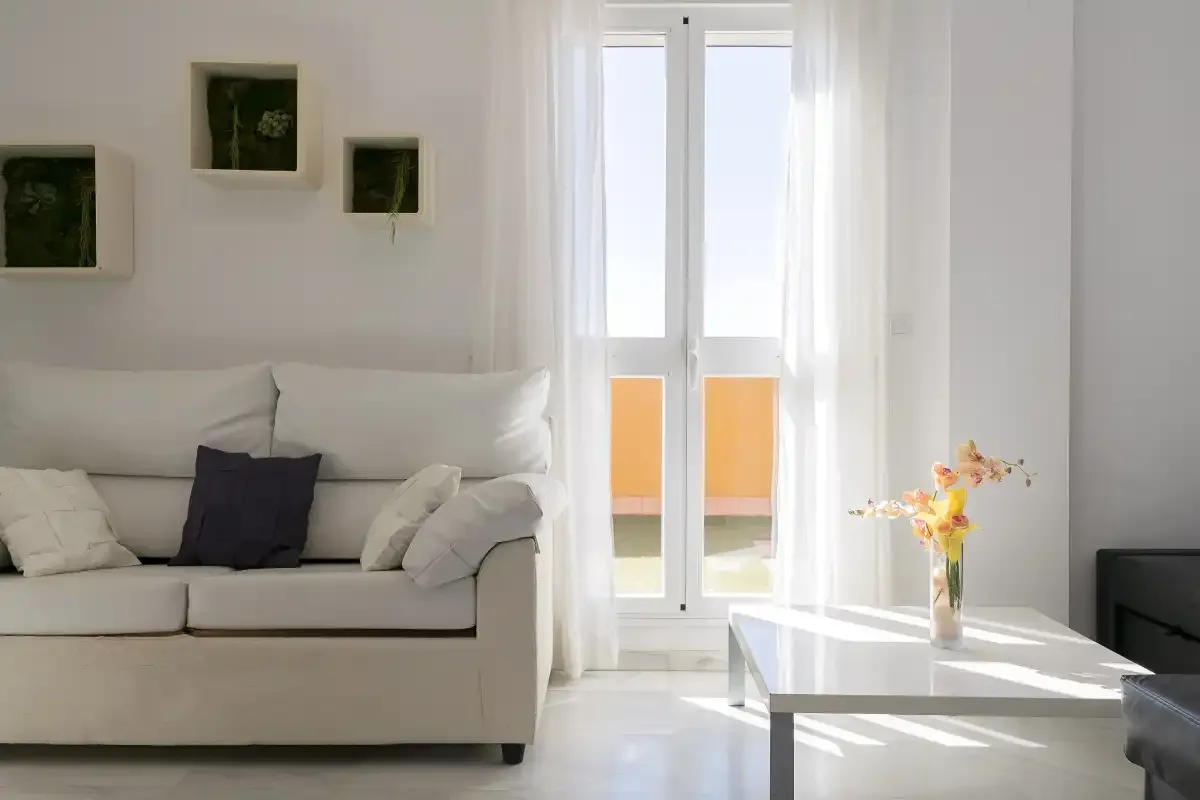 A bright living room with white seating beside tall glass doors.