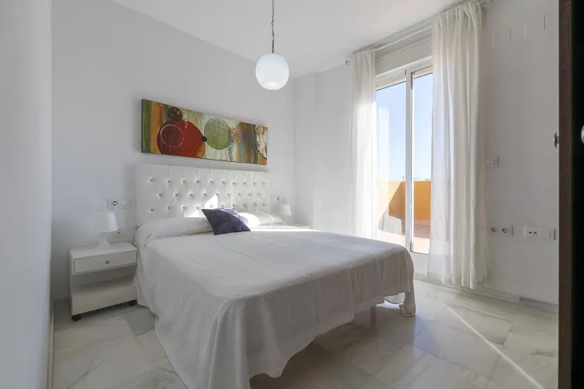 A bright bedroom with a neatly made bed and a large window.