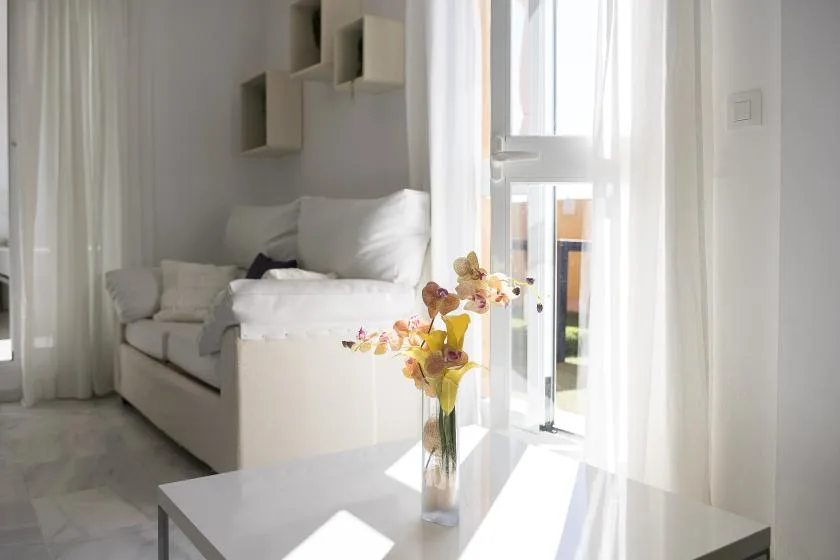 A bright living room with white seating and a small vase of flowers.