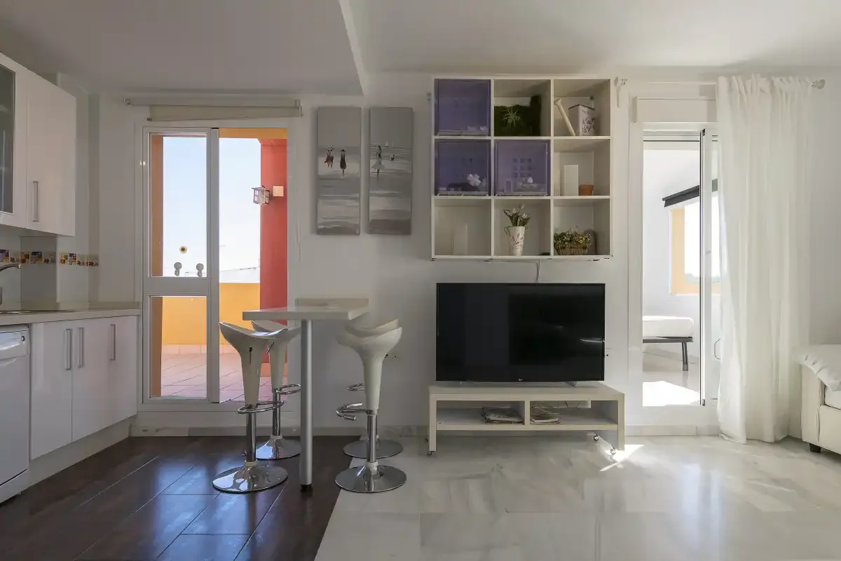 A bright open-plan kitchen and living area with a television and breakfast bar.