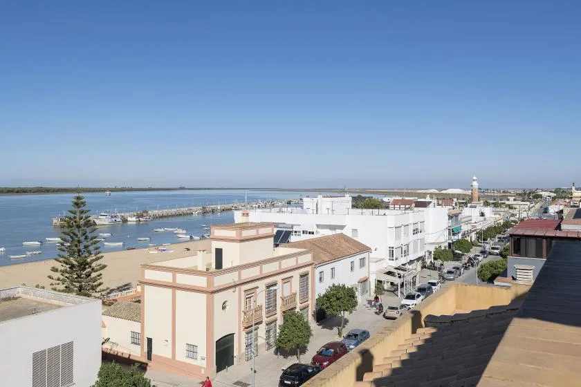 A waterfront town scene with boats in the harbor and buildings along the shore.