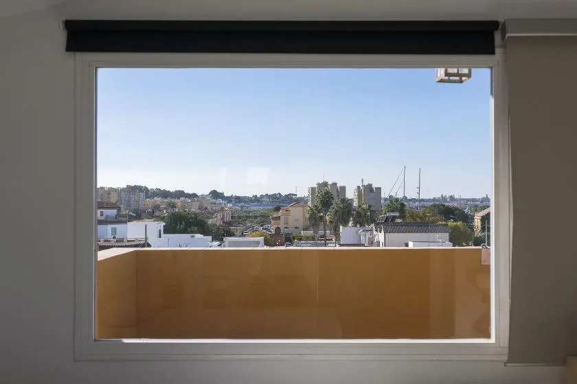 A large window overlooks a city skyline and nearby rooftops.