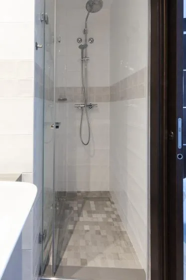 A tiled shower area with a wall-mounted showerhead and handheld spray.