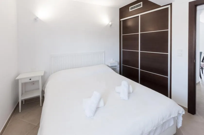A bright bedroom with a white bed and a dark sliding wardrobe.