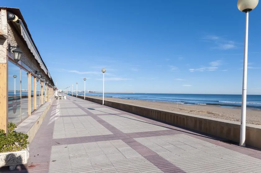 A seaside promenade runs beside a sandy beach and calm blue water.