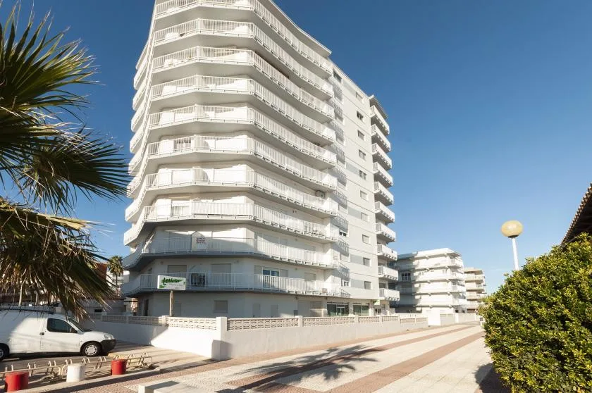 A tall white apartment building stands beside a sunny paved walkway.