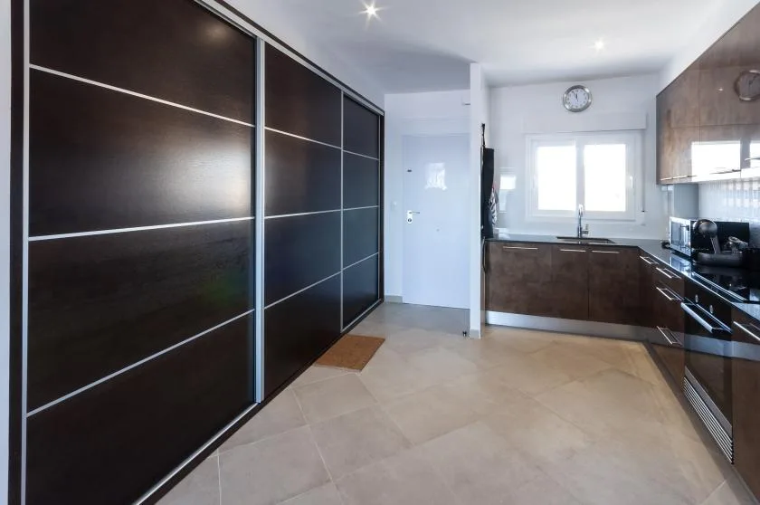 A modern kitchen with dark cabinetry, a window, and tiled flooring.