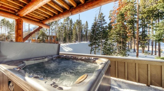 Una bañera de hidromasaje burbujeante está en una terraza cubierta con vistas a un bosque nevado.