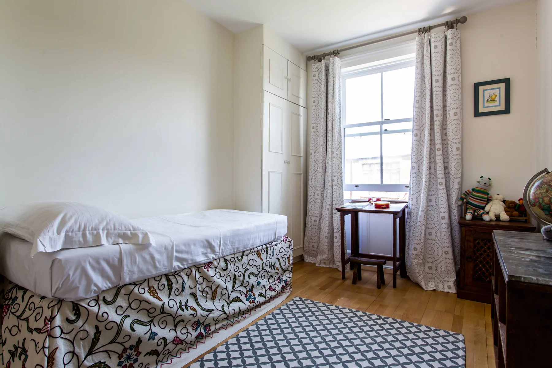 Un dormitorio con una cama junto a una ventana y una mesa pequeña.