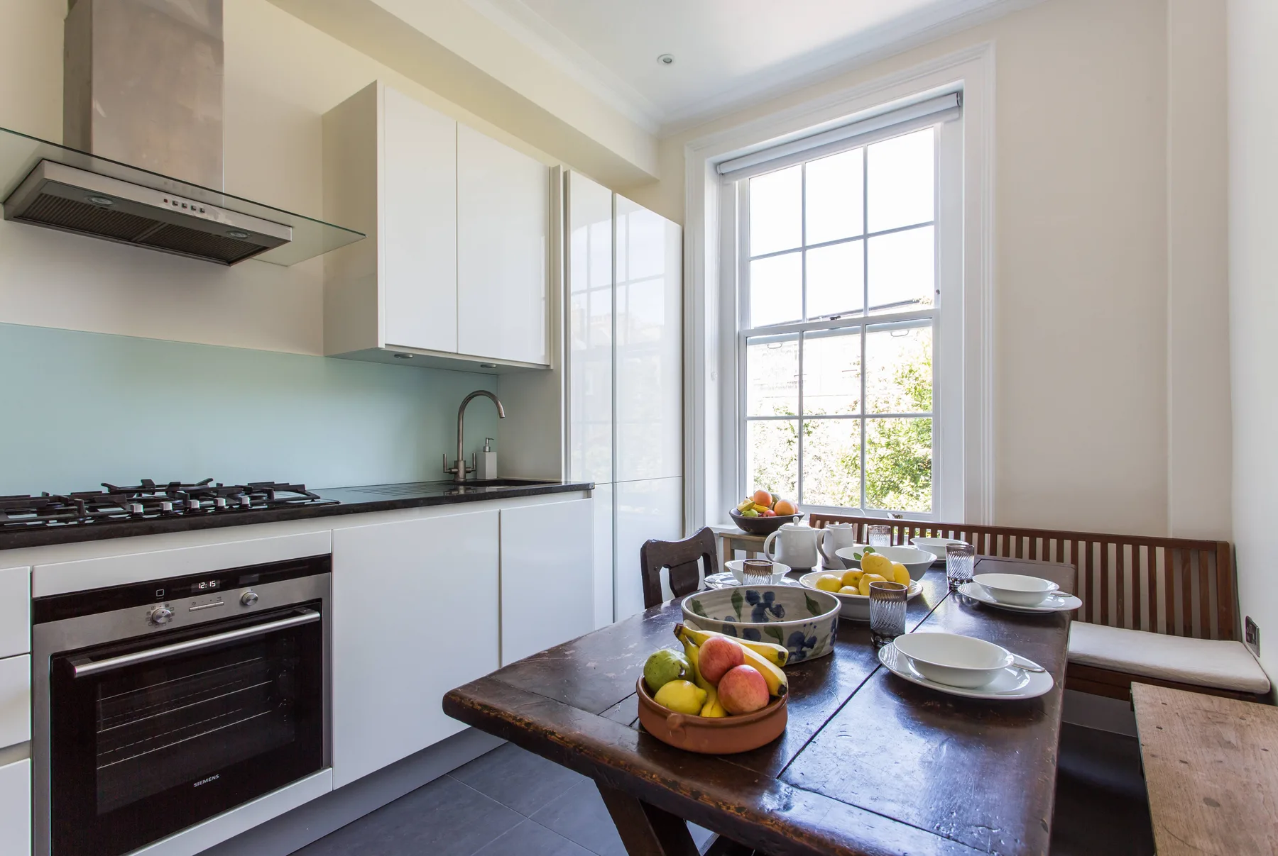 Una cocina luminosa con comedor y una mesa de madera junto a una ventana grande.